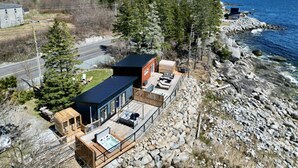Una propiedad costera con una casa principal, una casa de huéspedes y una terraza con mobiliario exterior.