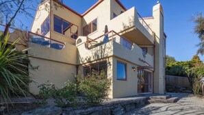 Una casa de dos pisos con base de piedra, múltiples ventanas y una escalera que lleva al piso superior.