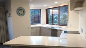 Una cocina moderna con una isla grande, dos taburetes de madera y vistas a un bosque a través de las ventanas.