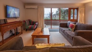Una sala de estar con una televisión, una mesa de centro de madera, un sofá a rayas, un sofá marrón y un puerta corrediza de vidrio que da a un balcón.
