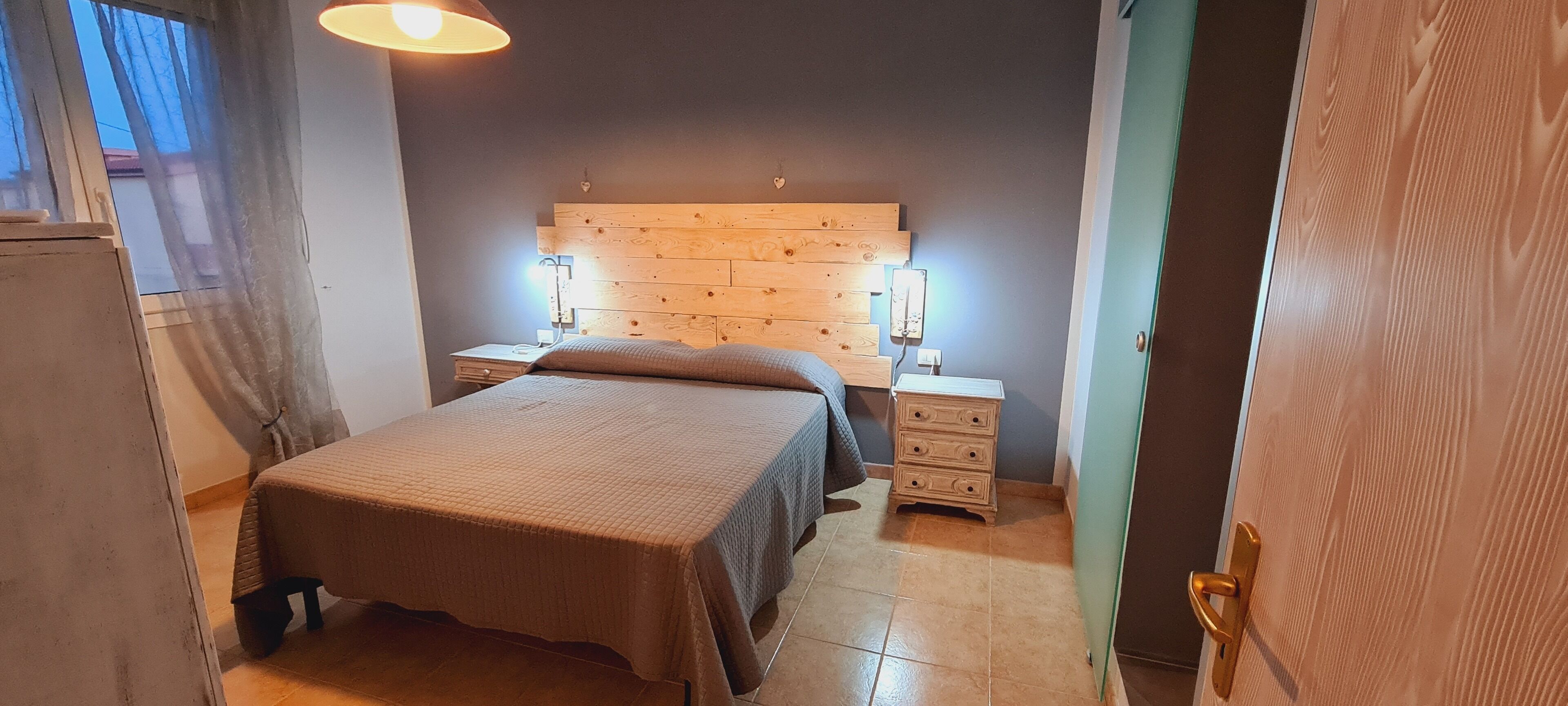 Un dormitorio con cabecera de madera, cama con colcha marrón, lámparas de noche, mesita de noche y cómoda.
