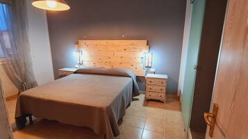 Un dormitorio con cabecera de madera, cama con colcha marrón, lámparas de noche, mesita de noche y cómoda.