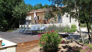 A villa with a wooden deck, outdoor seating, and a garden with flowers. - Farmhouse for 6 people with heated swimming pool, jacuzzi, sauna south of France (Labastide de Virac)