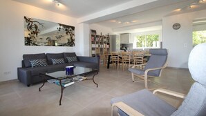A spacious living area with a sofa, coffee table, and armchairs. A bookshelf and dining area are visible in the background. - Farmhouse for 6 people with heated swimming pool, jacuzzi, sauna south of France (Labastide de Virac)