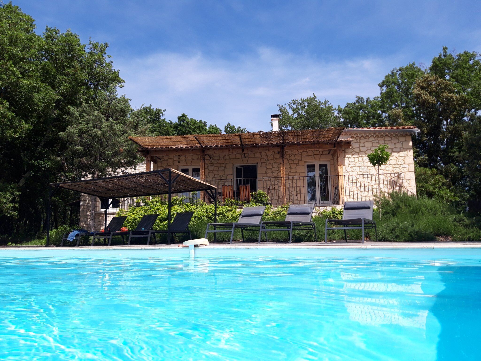A stone building with a pool, sun loungers, and a covered seating area.