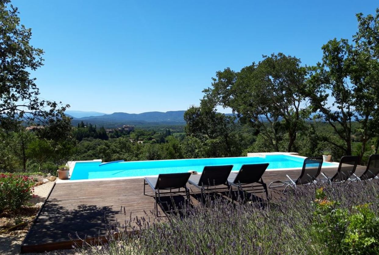 Ein Pool mit Liegestühlen, umgeben von viel Grün und Bergen im Hintergrund.
