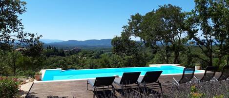 Ein Pool mit Liegestühlen, umgeben von viel Grün und Bergen im Hintergrund.