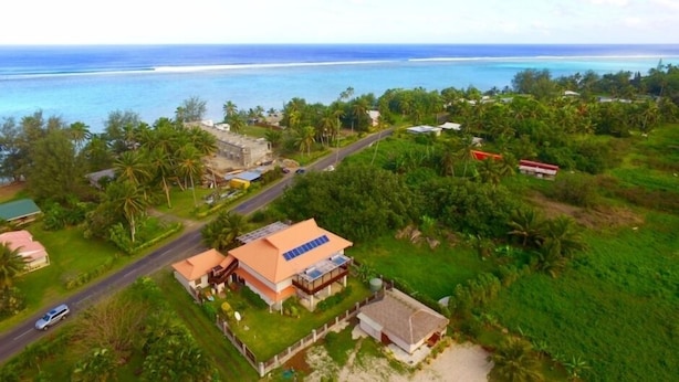 Luchtbeeld van een kustbezit met een weg, een huis met zonnepanelen en uitzicht op de oceaan.