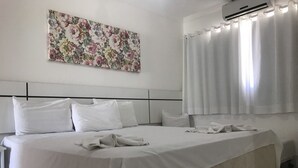 Een hotelkamer met een groot bed, een hoofdbord, een bloemrijk kunstwerk aan de muur en een airconditioner.