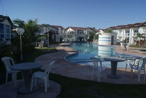 Un espace piscine aménagé avec des chaises longues et une petite table, entouré d’immeubles dotés de balcons.