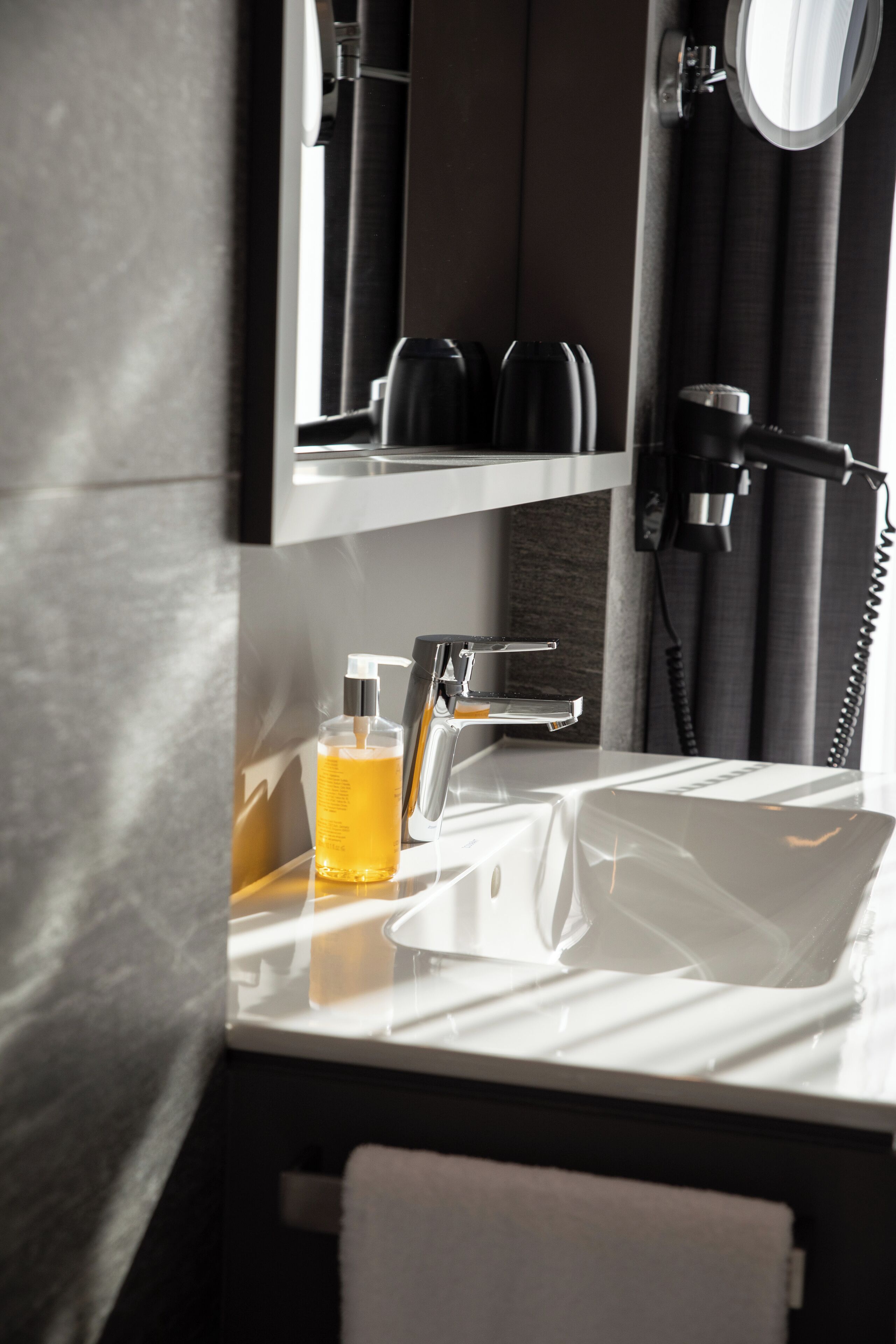 A modern bathroom with a white sink, a mirror, and a bottle of yellow liquid.