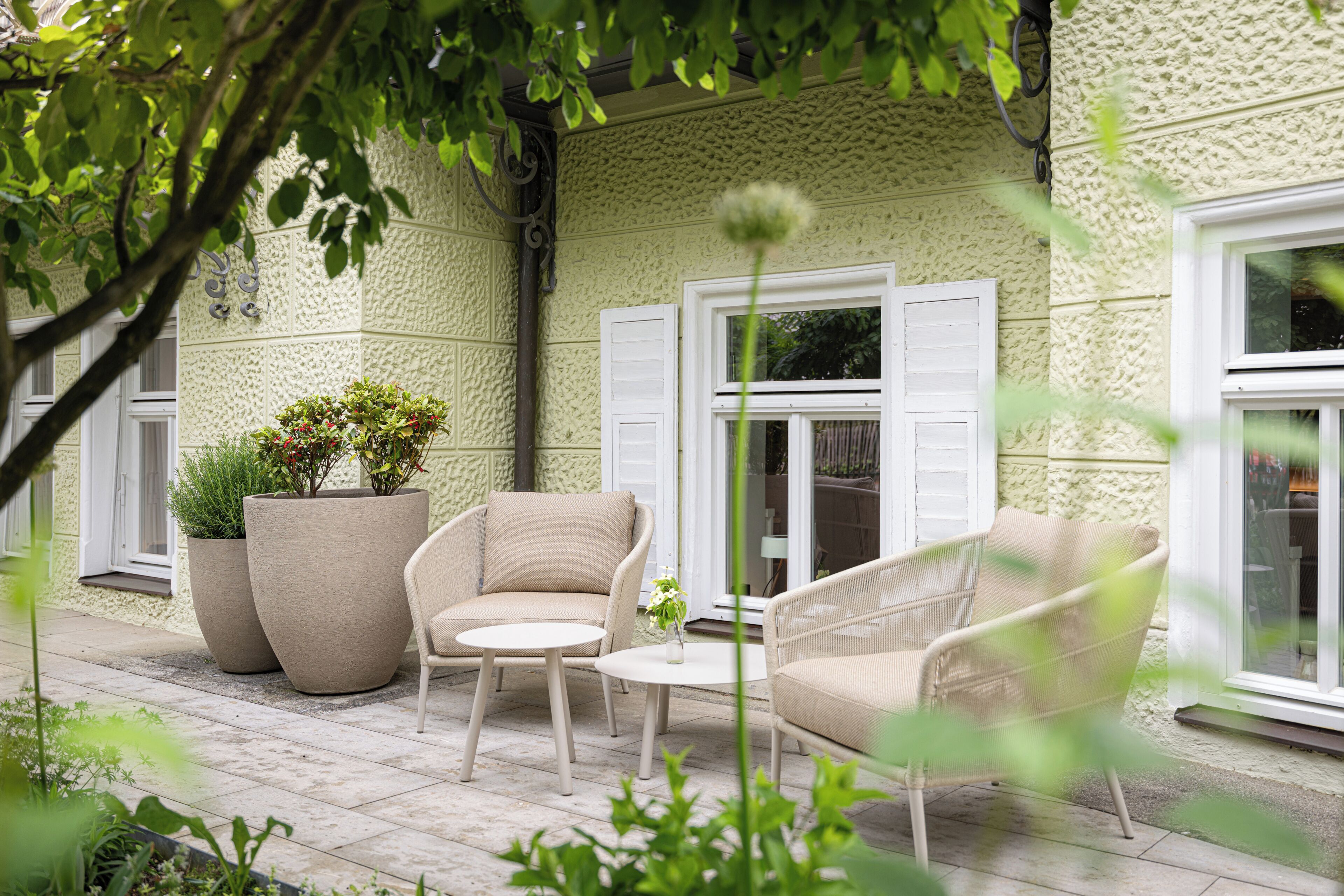 A patio with outdoor furniture, a potted plant, and a window with shutters.