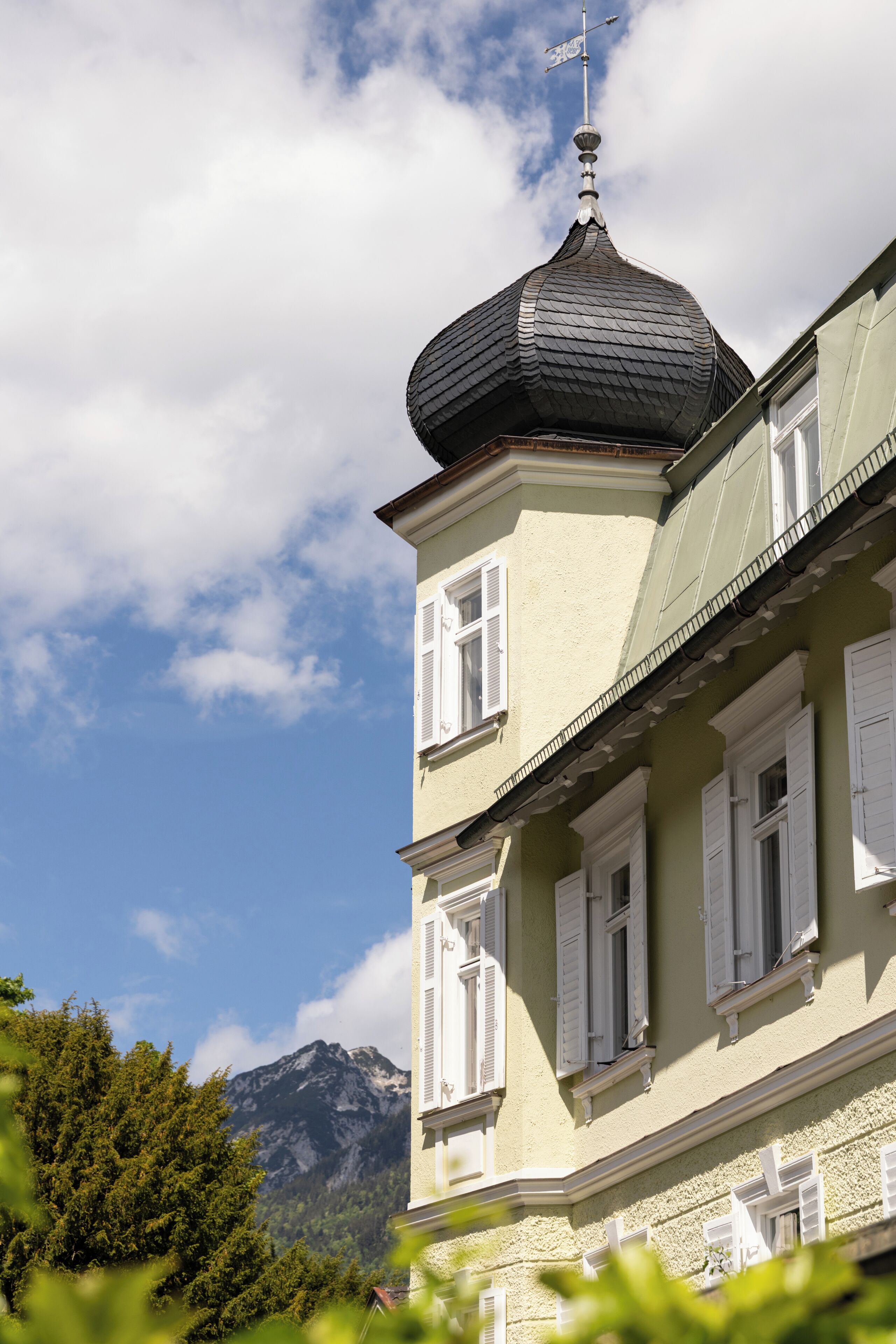 A building with a prominent dome and multiple windows, set against a mountainous backdrop.