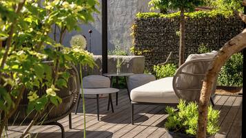 A wooden deck with outdoor furniture, a pergola, and lush greenery.