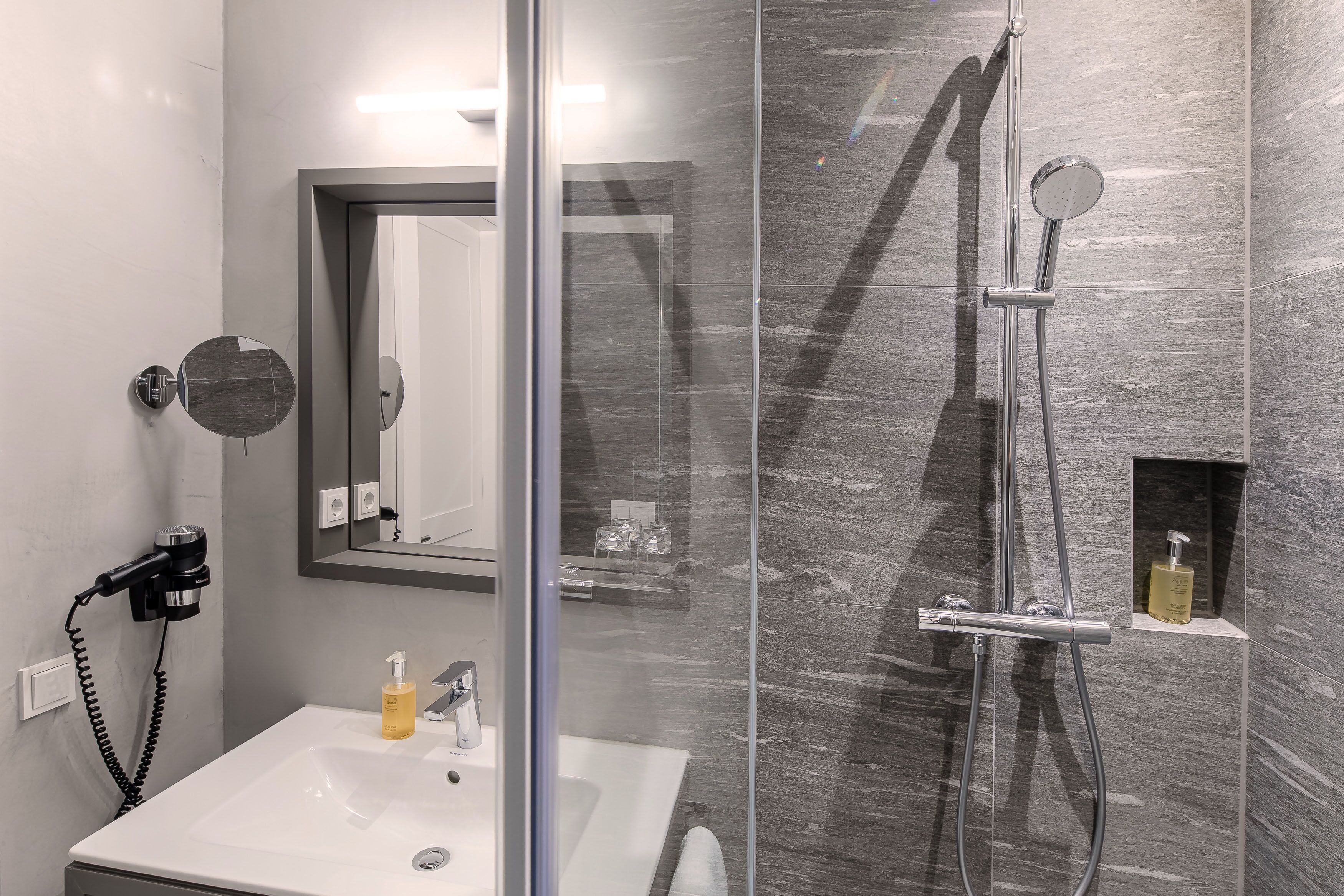 Un baño moderno con ducha de vidrio, lavamanos blanco y un espejo.