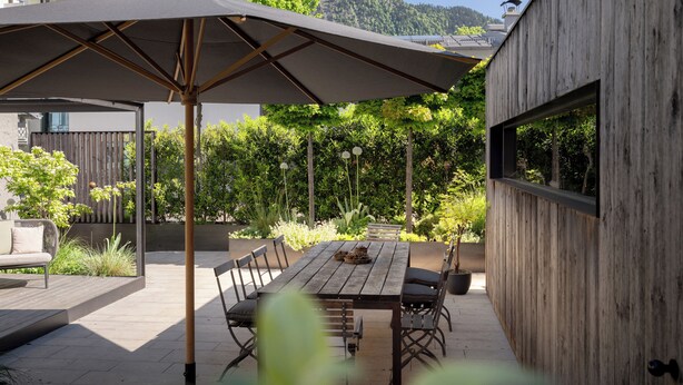 An outdoor patio with a wooden table, chairs, and a large umbrella. - Villa Rein Boutiquehotel (Bad Reichenhall)
