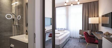 A modern hotel room with a shower, a bed, a desk, and a chair.