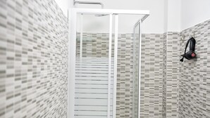 Une douche avec une porte en verre, des murs carrelés et un sèche-cheveux fixé au mur.