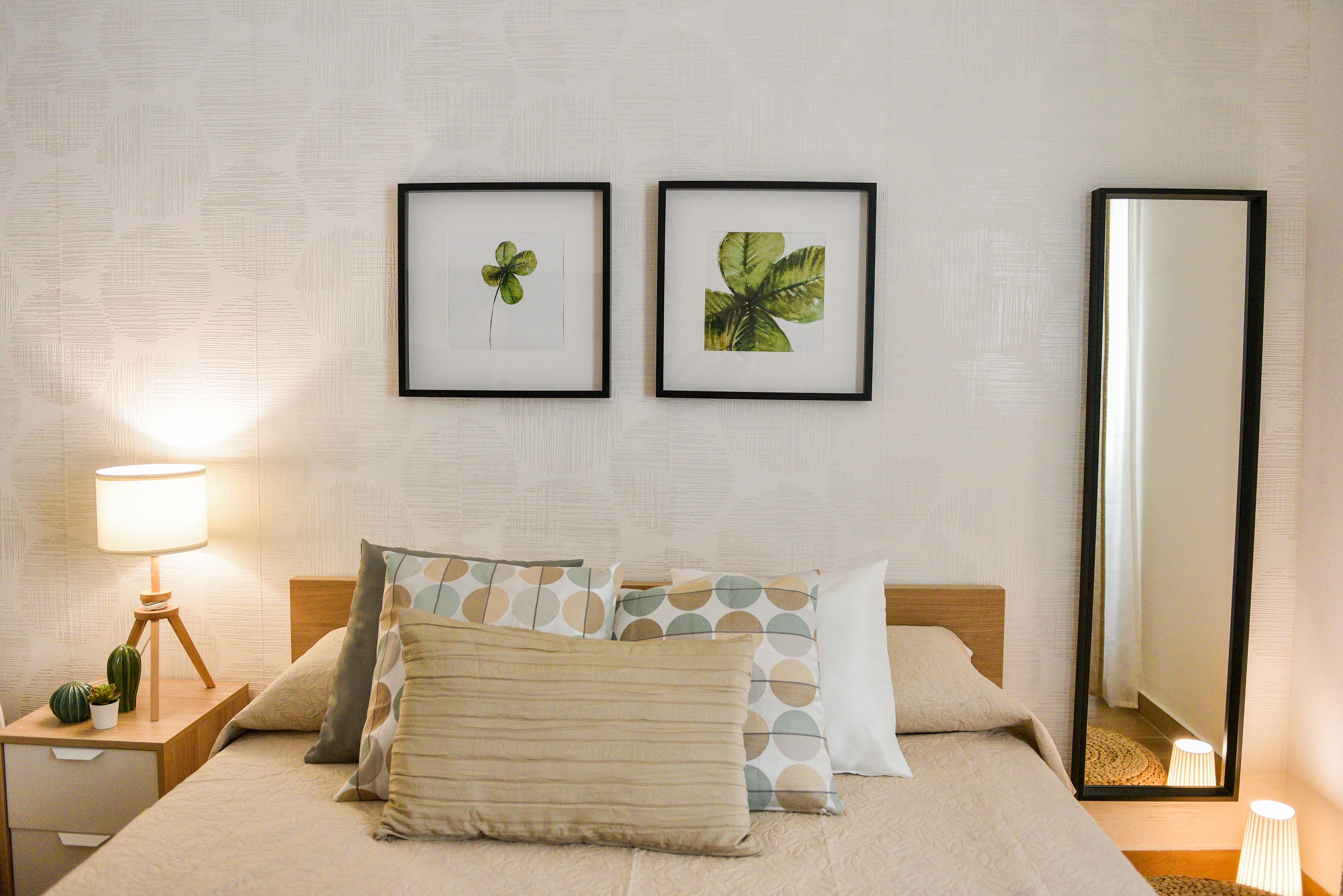 Habitación de hotel ordenada con cama, almohadas, mesita de noche con lámpara y dos cuadros en la pared.