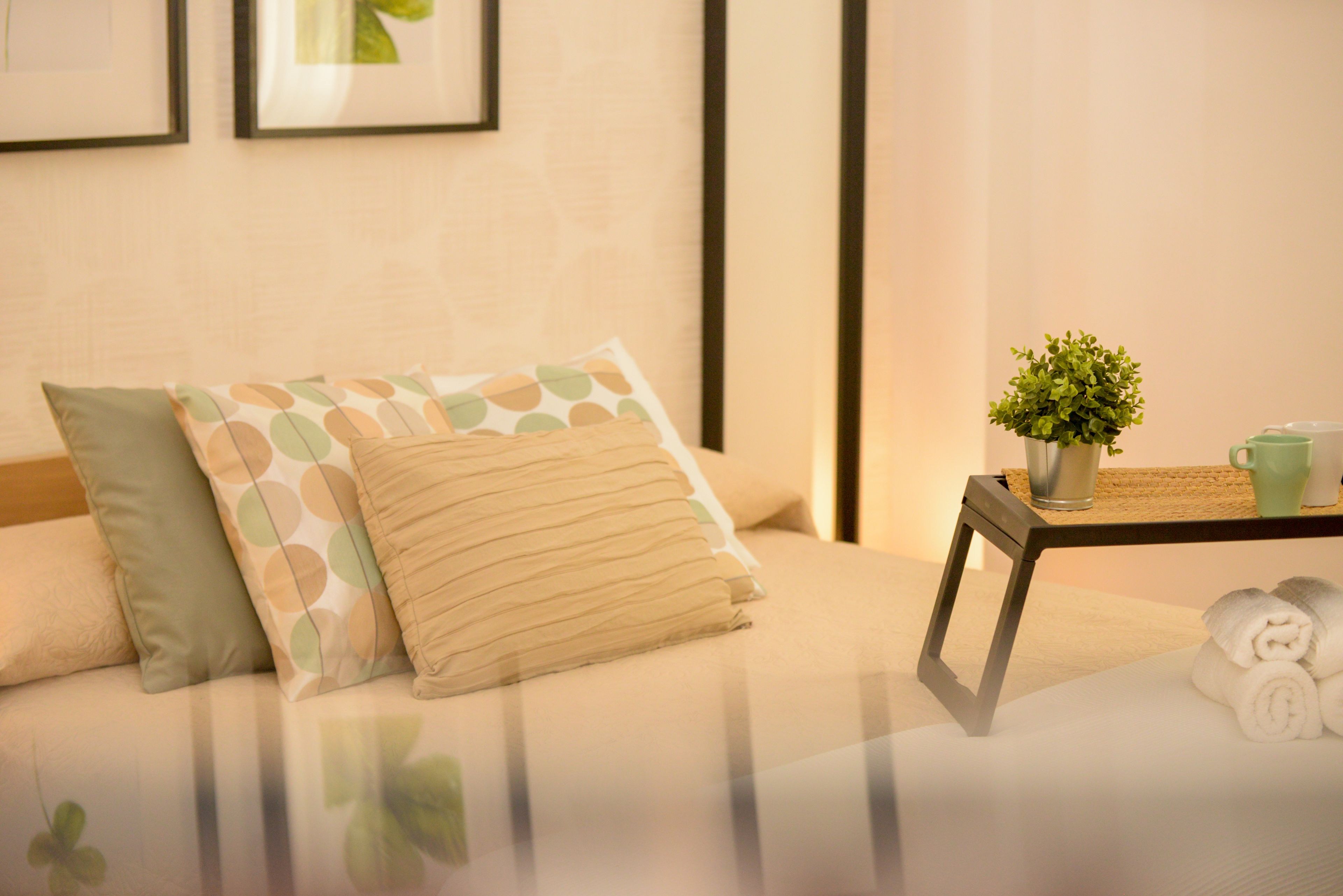 A neatly arranged hotel room with a bed, pillows, a small table with a plant and a cup, and a framed picture on the wall.