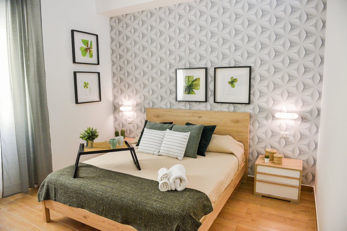 Ein ordentlich eingerichtetes Schlafzimmer mit einem hölzernen Bett, einem Nachttisch und einer Wand mit geometrischem Muster.