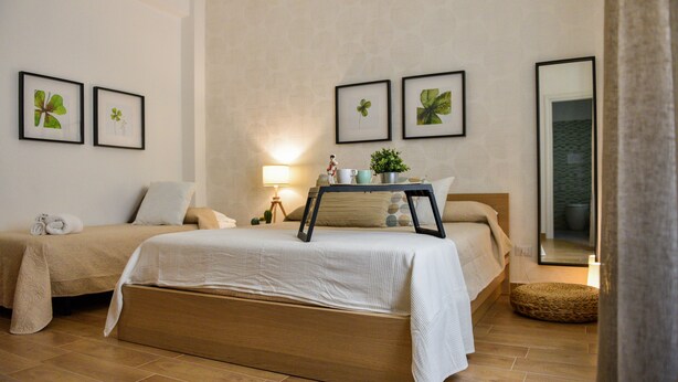 Une chambre avec deux lits, une table de chevet avec une lampe, des reproductions botaniques encadrées accrochées au mur et un grand miroir.