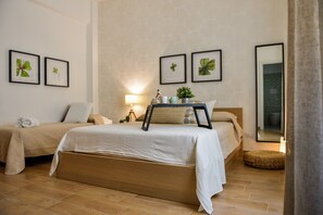 Une chambre avec deux lits, une table de chevet avec une lampe, des reproductions botaniques encadrées accrochées au mur et un grand miroir.