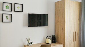 Une petite pièce moderne, équipée d’un bureau en bois, d’une chaise, d’un téléviseur, d’une armoire et d’un radiateur.