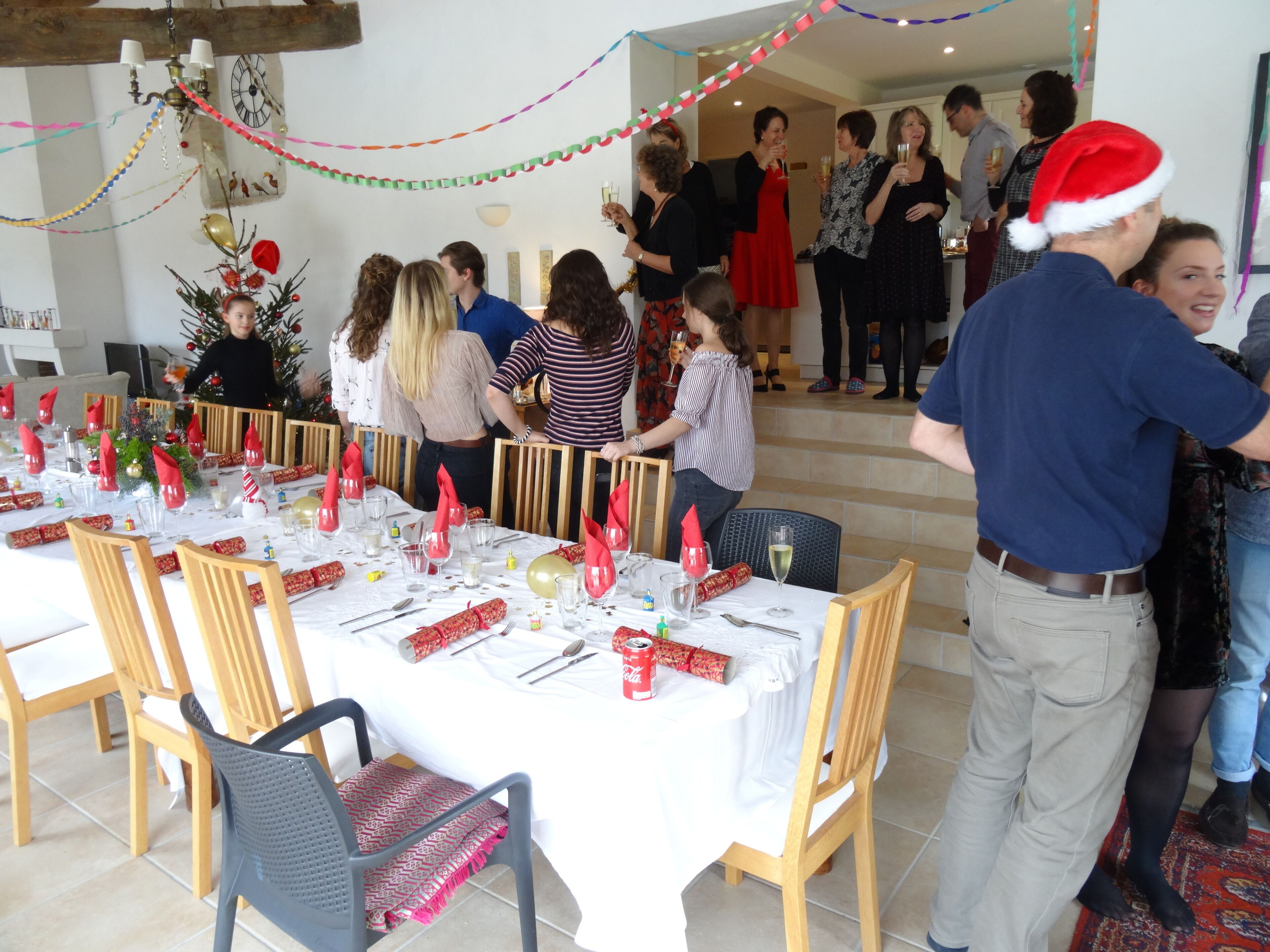Un comedor con mesas dispuestas para una comida, sillas y un árbol de Navidad al fondo.