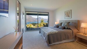 A bedroom with a large bed, a nightstand, a lamp, and a view of mountains and a lake.