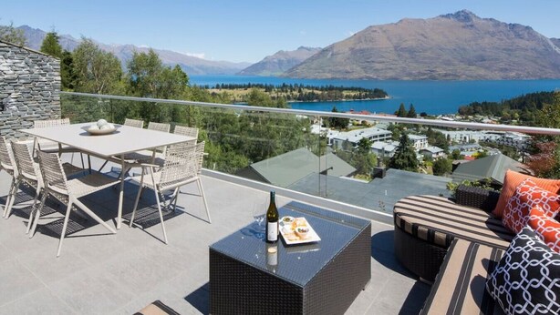 A balcony with a table and chairs, a wicker sofa, and a bottle of wine.