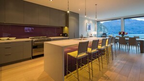 A modern kitchen with a central island, bar stools, and a view of the sea.
