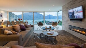 A modern living room with a sofa, coffee table, and chairs, a flat-screen TV, and a fireplace.