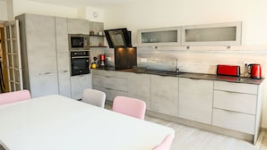 Et moderne køkken med indbyggede apparater, et spiseområde med et hvidt bord og pink stole, samt et stort vindue over vasken.