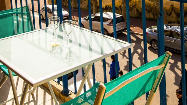 En balkon med et glasbord og stole, der vender ud mod en havn med både og bygninger.