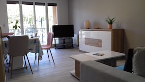 En moderne stue med et fladskærms-tv, et spiseområde med en lyserød stol, og en potteplante på et træskab.