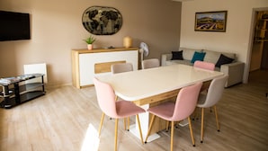 En moderne stue med spiseplads, sofa, fjernsyn og et maleri på væggen.