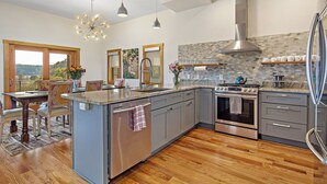 A modern kitchen with a central island, stainless steel appliances, and a large window overlooking a scenic landscape. - Upstream Bachelorette Oasis - DOWNTOWN LOCATION! (Asheville)