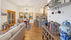 A spacious living room with a large sofa, wooden flooring, and a dining area with chairs and a table. - Upstream Bachelorette Oasis - DOWNTOWN LOCATION! (Asheville)