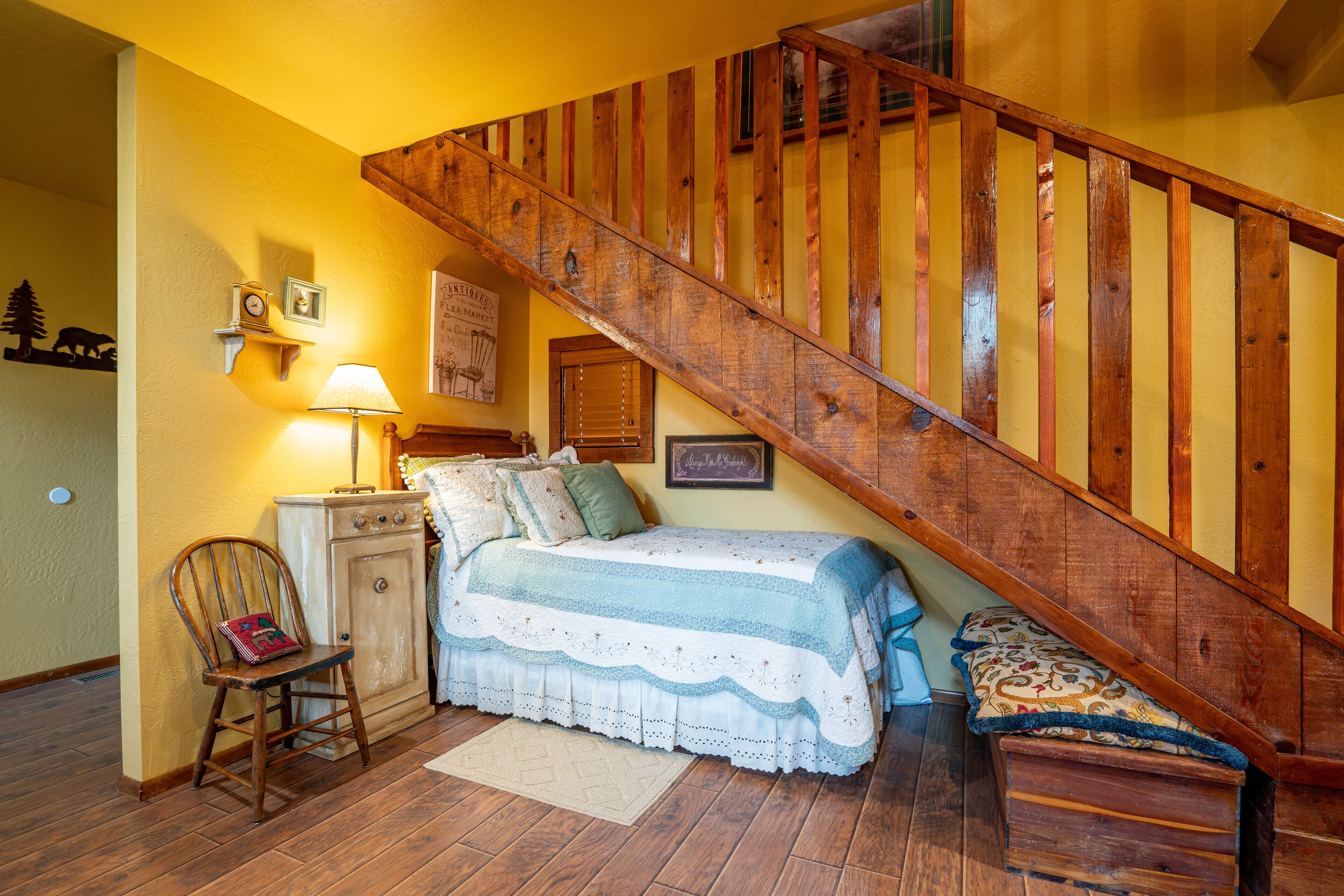 A bedroom with a wooden staircase, a bed with a blue and white bedspread, a wooden chair, a nightstand, and a lamp.