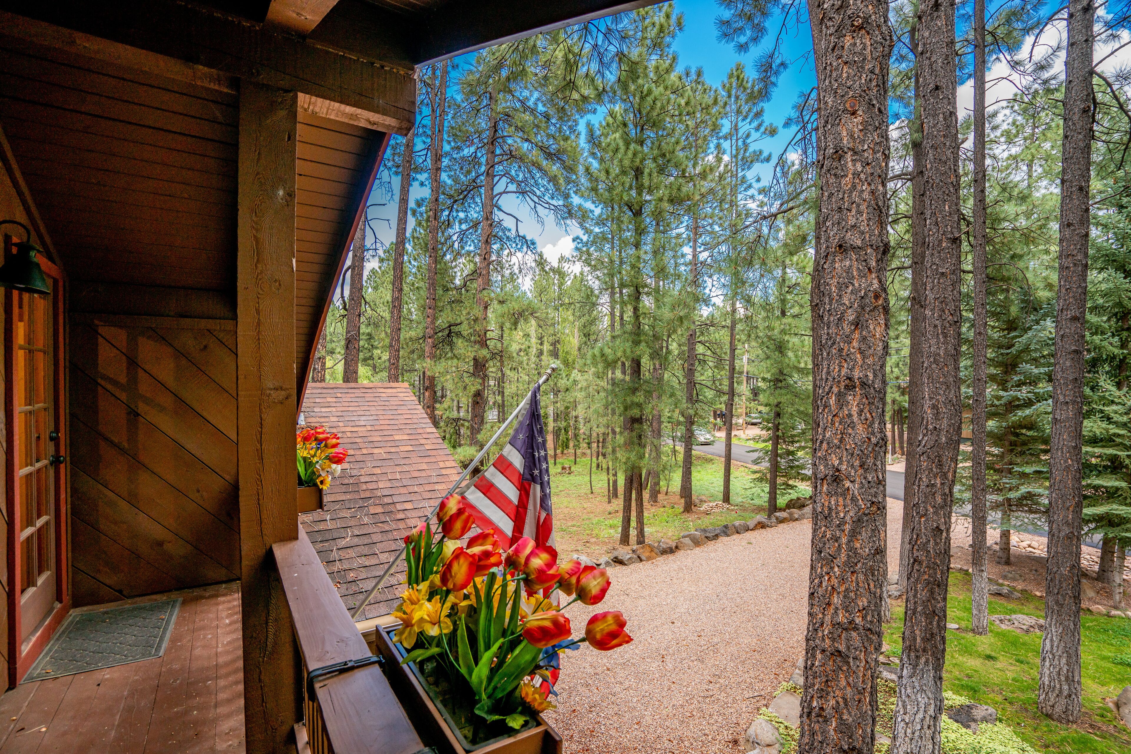 Une cabane en bois avec un porche, un drapeau et une jardinière remplie de tulipes.