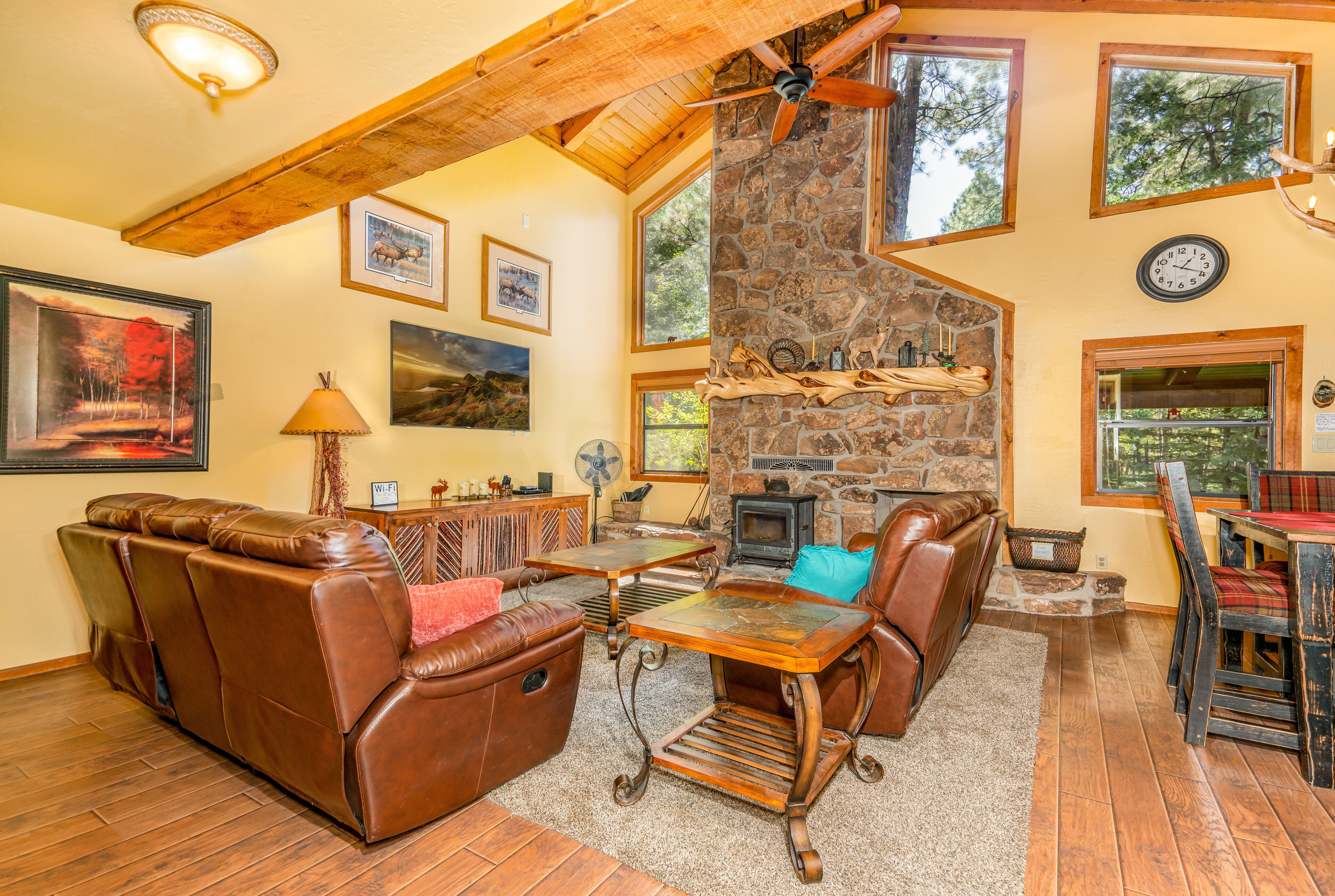 A cozy living room with a stone fireplace, leather furniture, and large windows offering views of the outdoors.
