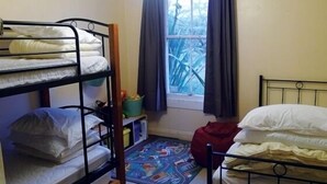 Une chambre de dortoir avec des lits superposés, une fenêtre avec des rideaux, un petit tapis et une étagère avec quelques objets.