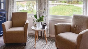 A room with two beige armchairs, a small white table with a potted plant, and a view of a green lawn through large windows. - Nice home in Vesterøy with WiFi (Vesterøy)
