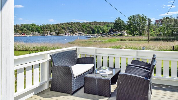 A deck with wicker furniture and a view of a lake and forest. - Nice home in Vesterøy with WiFi (Vesterøy)