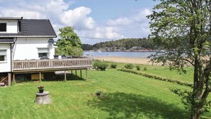A white house with a deck overlooking a lake, surrounded by greenery and a clear sky. - Nice home in Vesterøy with WiFi (Vesterøy)