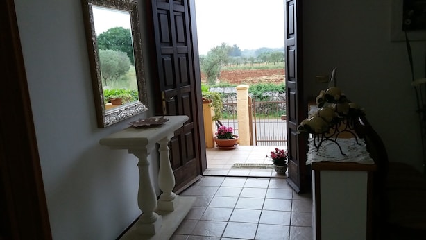A hallway with a tiled floor, a white console table, a mirror, and a door leading to a balcony with potted plants. - Villetta Orchidea (Giuggianello)