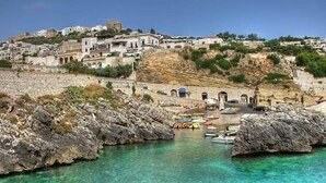 A coastal town with buildings on a hillside, a rocky shoreline, and boats in the water. - Villetta Orchidea (Giuggianello)