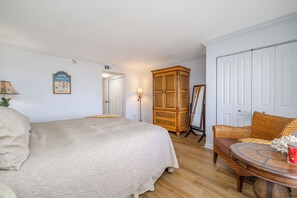 Une chambre à coucher avec un lit, une armoire en bois, une chaise en osier, une table et une porte.