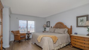 A bedroom with a large bed, a chair, a dresser, and a window with blinds.